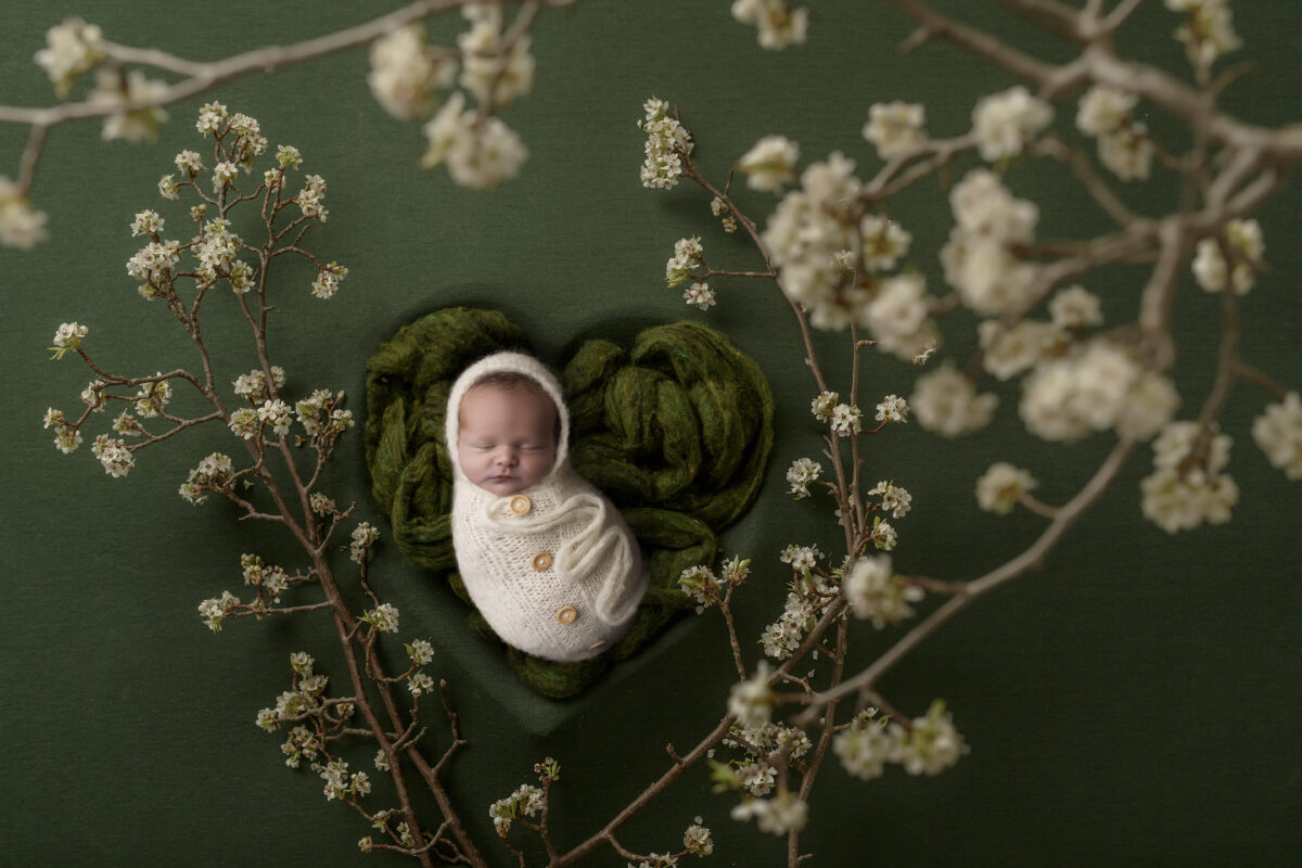 newborn baby with white flowers and white wrap with buttons in green heart