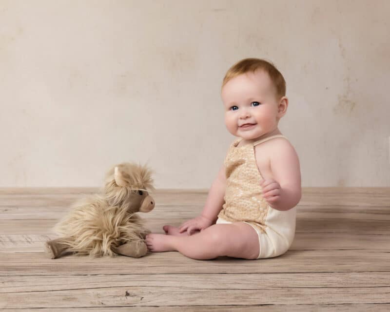 baby girl sitting on wood with cow toy