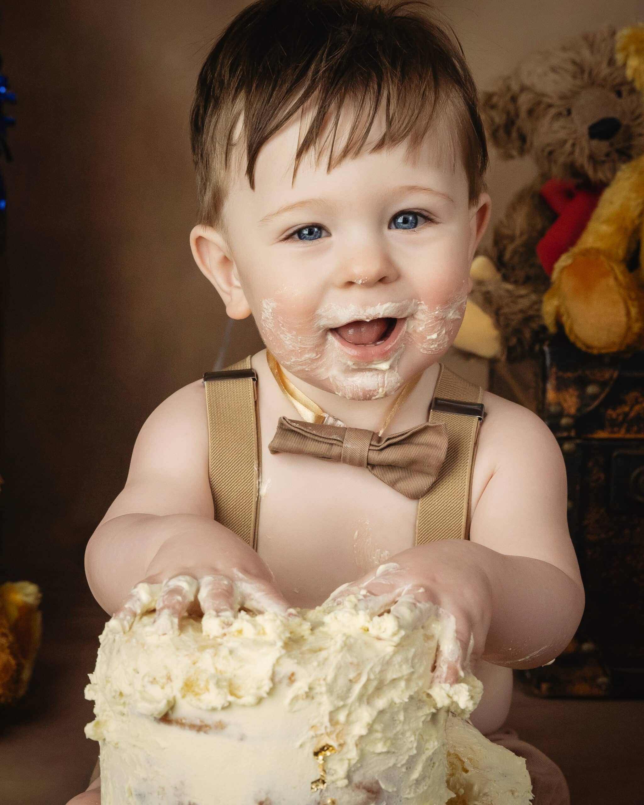 baby in brown overalls and bow tie eating birthday cake