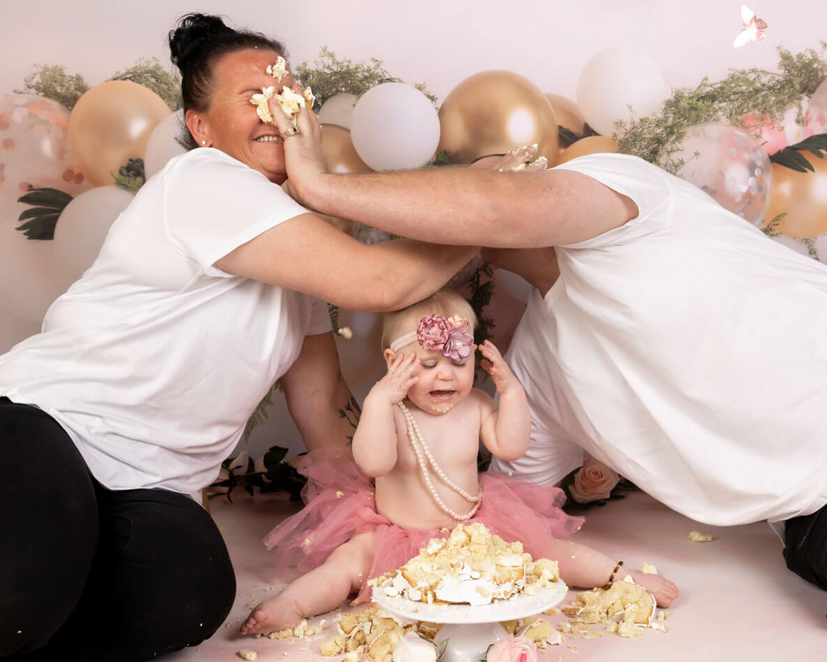 mum and dad smashing cake with baby in pink tutu