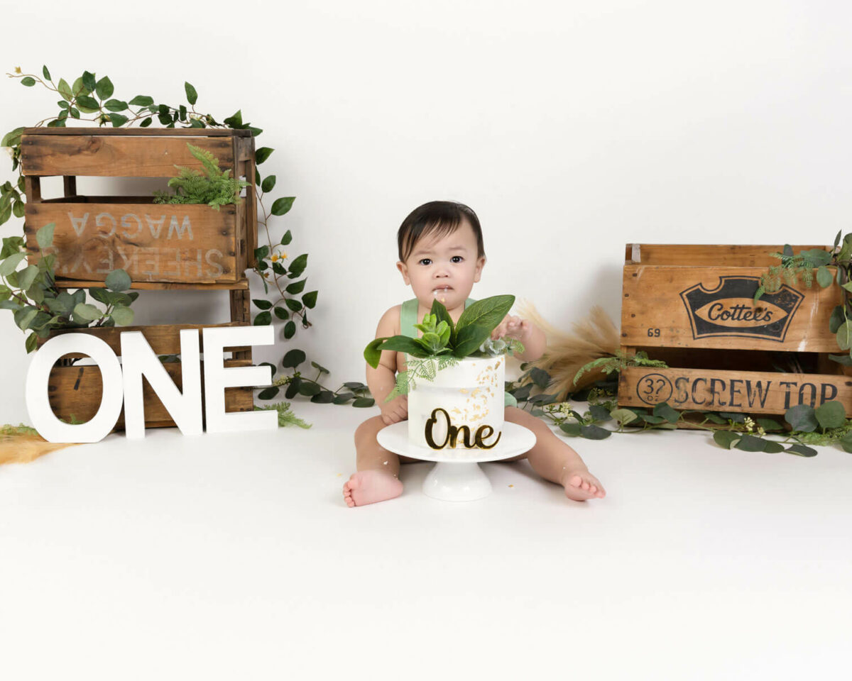 baby in green overalls with leaves and boxes eating birthday cake