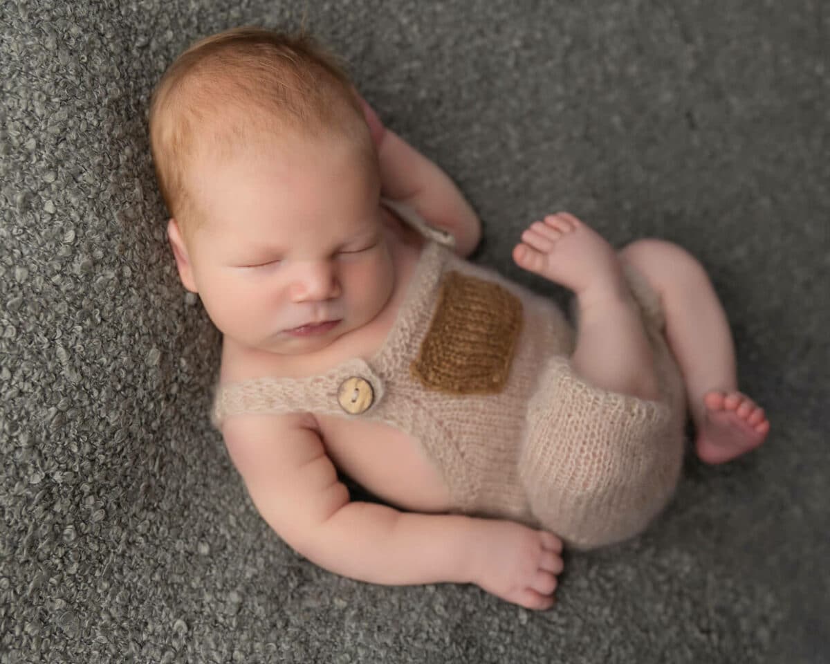 newborn baby in overalls sleeping on grey