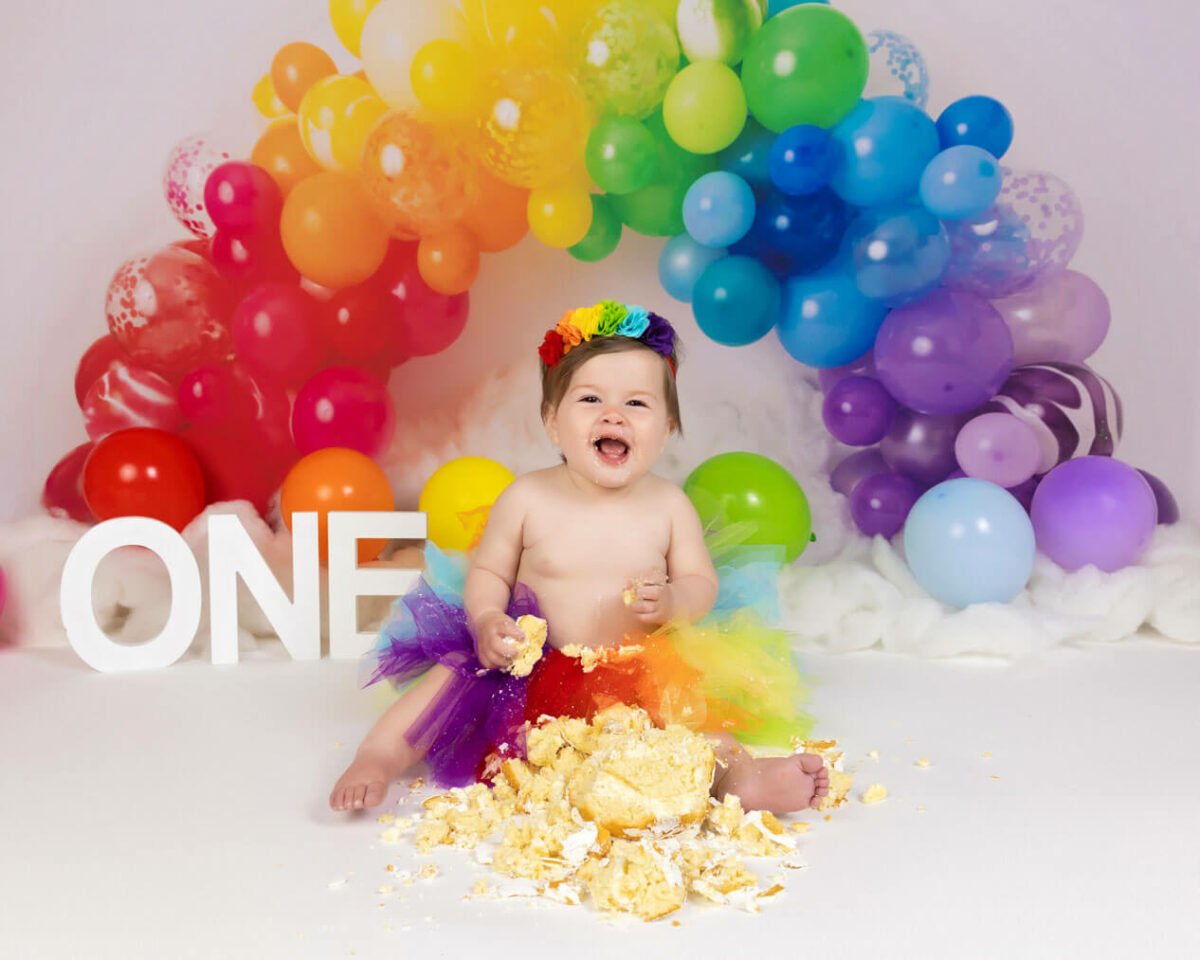 Baby with rainbow balloons happy eating birthday cake