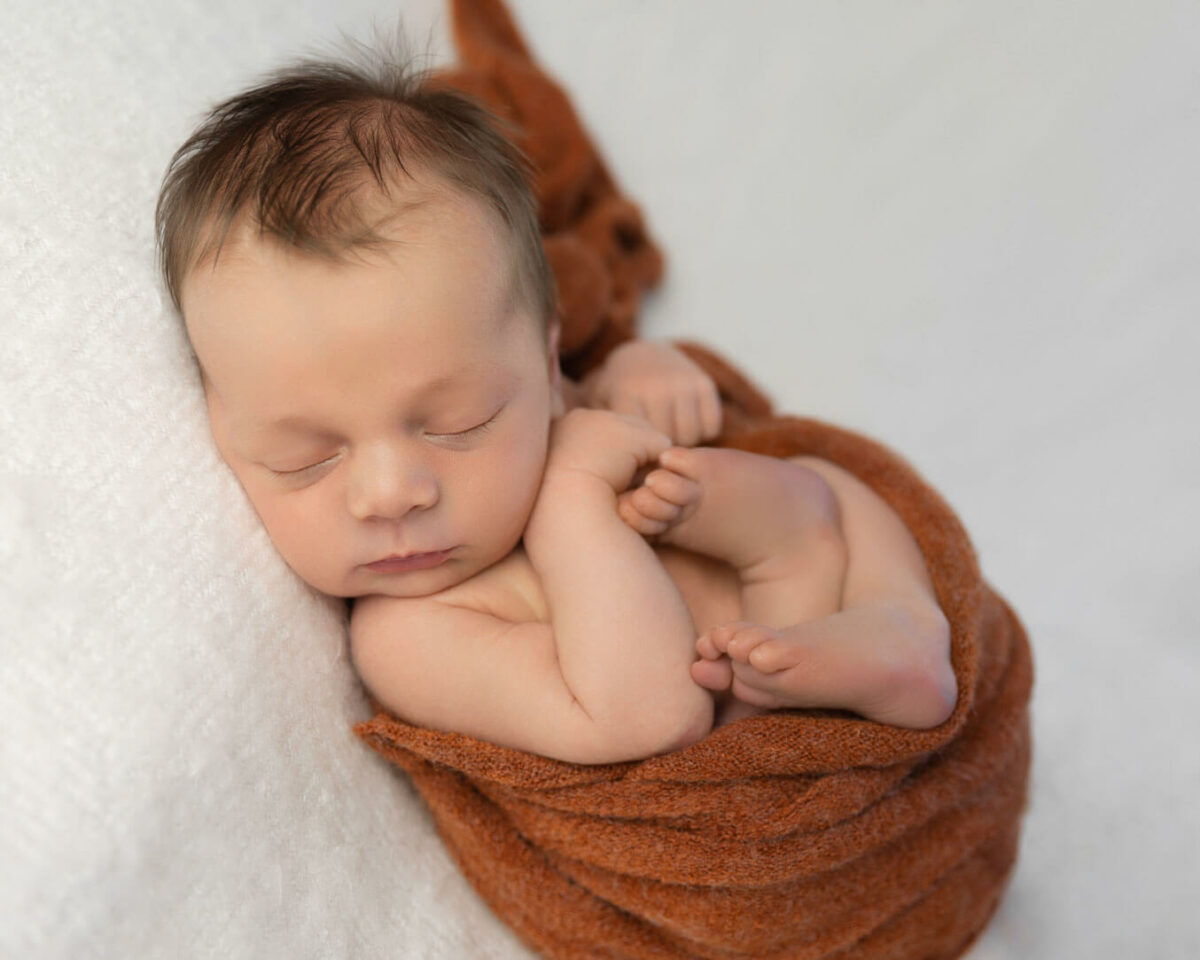 newborn baby sleeping wrapped up in rust wrap